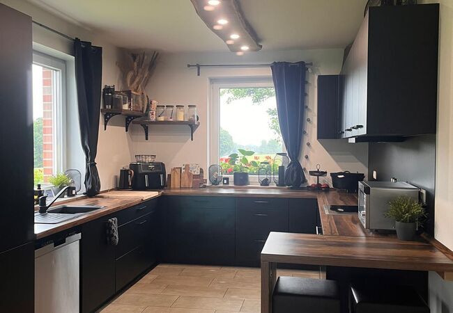 Ansicht der fertig und aufgebauten Küche mit Küchenschrank in dunkler Farbe mit Arbeitsplatte und Schubladen, sowie Fenster im Hintergrund